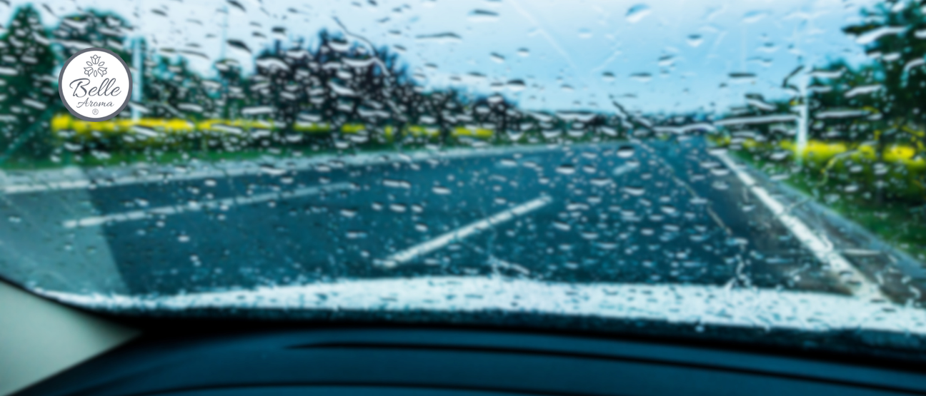 Rain-speckled windshield view from inside a car driving along a highway, capturing a moody travel moment. Ideal for road trip storytelling, aromatherapy travel inspiration, and scent-enhanced driving experiences with Belle Aroma.