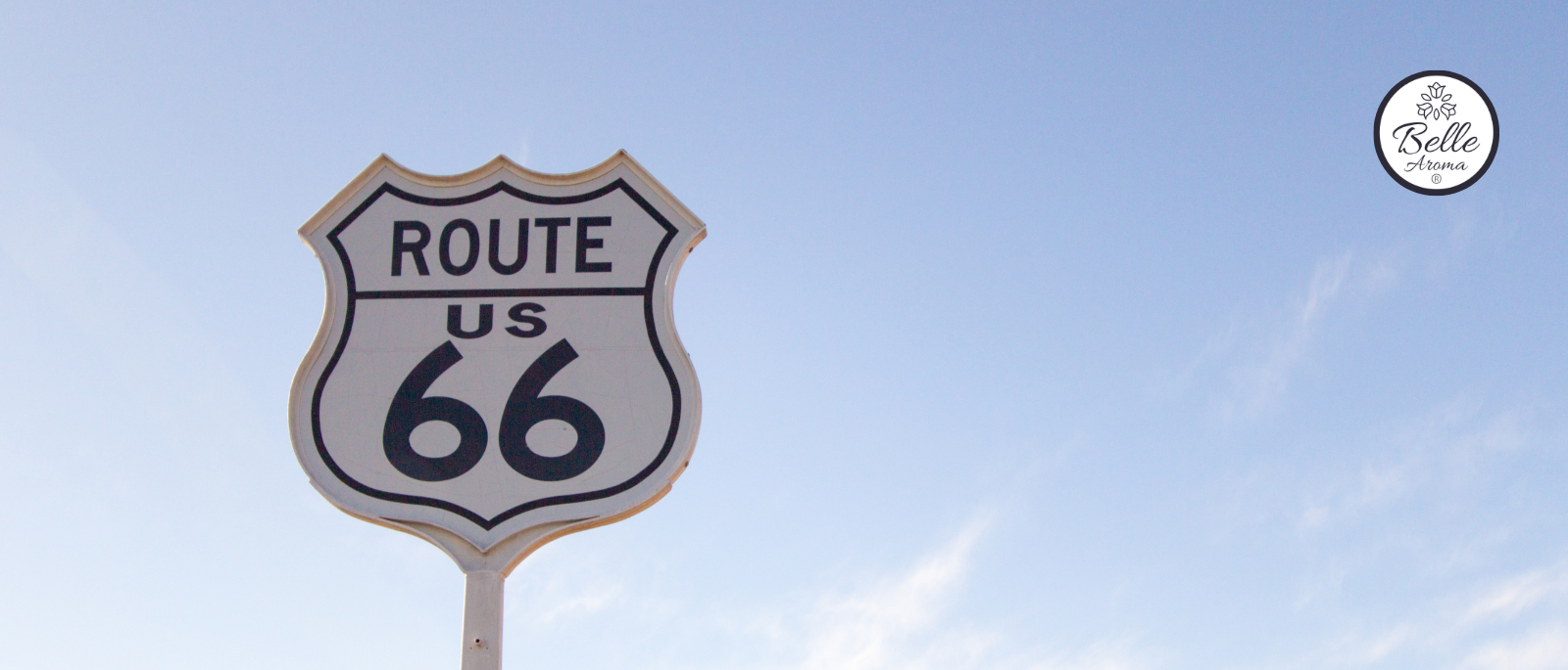 Route 66 highway sign against a bright blue sky for Belle Aroma® Scents of Adventure blog. Nostalgic road trip imagery inspired by travel, adventure, and the classic American Mother Road experience.